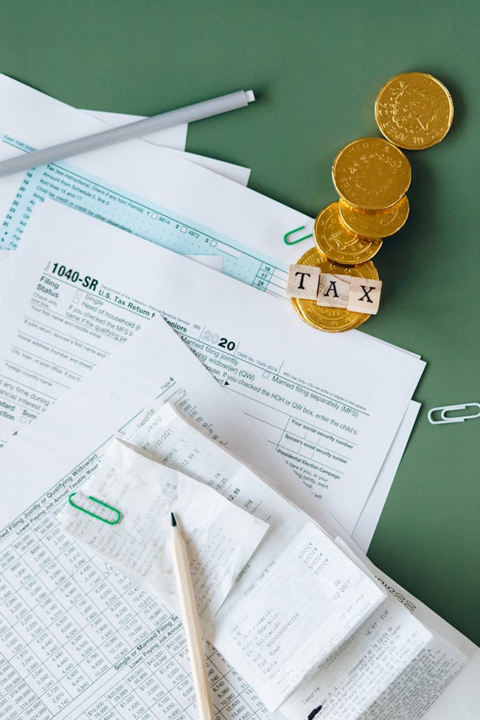 Tax documents and gold coins on a green desk symbolizing financial planning and savings.